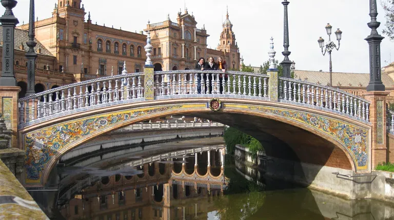 Students stand on an intricate bridge over a river in Seville, Spain